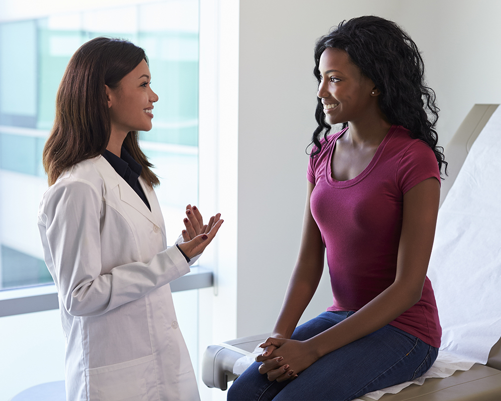 woman sitting on table at doctor's office talking to nurse