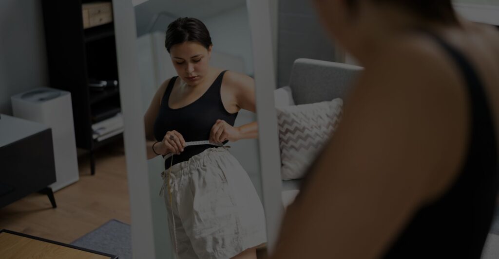 Woman measuring waist in the mirror